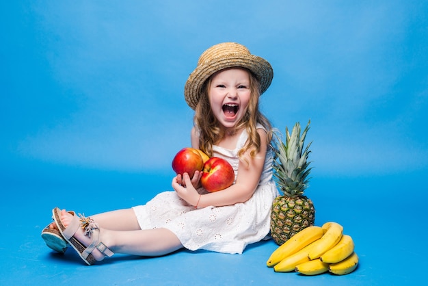 Śliczna mała dziewczynka z owocami na białym tle na niebieskiej ścianie