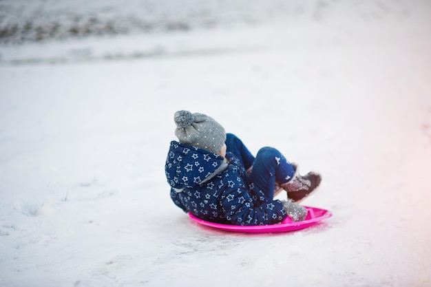 Śliczna mała dziewczynka ze spodkami na saniach na zewnątrz w zimowy dzień