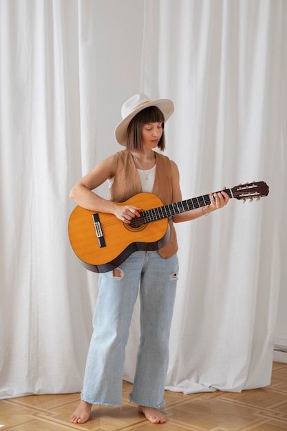 Śliczna młoda kobieta gra na gitarze w pomieszczeniu