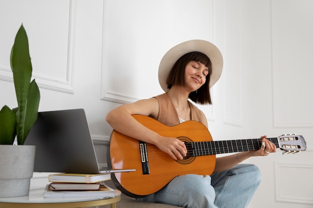 Bezpłatne zdjęcie Śliczna młoda kobieta gra na gitarze w pomieszczeniu