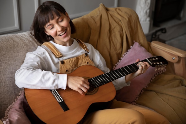 Bezpłatne zdjęcie Śliczna młoda kobieta gra na gitarze w pomieszczeniu