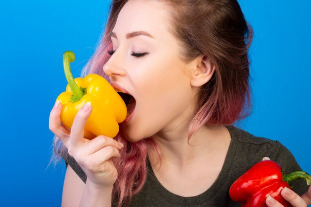 Śliczna młoda kobieta gryźć żółtego pieprzu z różowym włosy