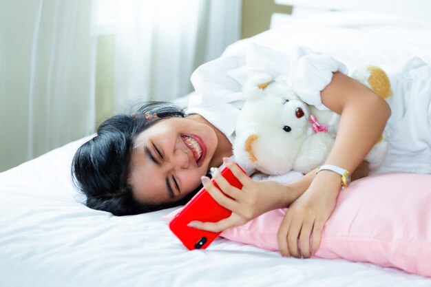 Śliczna nastoletnia kobieta radosna z smartphone na łóżku