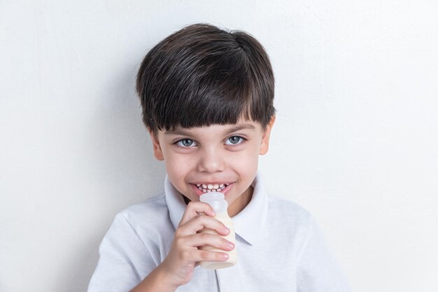 Śliczny chłopiec w białej koszuli na białym tle pije sfermentowane mleko