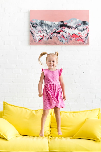 Bezpłatne zdjęcie Śliczny dziewczyny doskakiwanie na żółtej kanapie