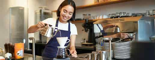 Bezpłatne zdjęcie słodka brunetka, barista, personel kawiarni, nalewający wodę z czajnika i piwa, filtrująca kawę