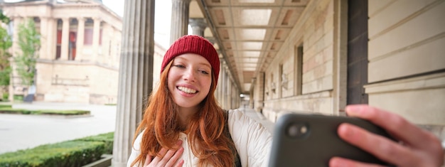 Bezpłatne zdjęcie słodka młoda rudowłosa kobieta robi sobie selfie na ulicy za pomocą telefonu komórkowego