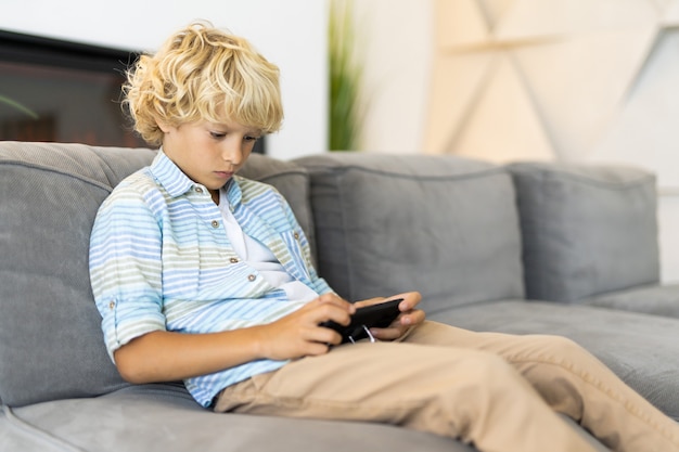 Słodki chłopak grający w gry wideo na smartfonie w domu