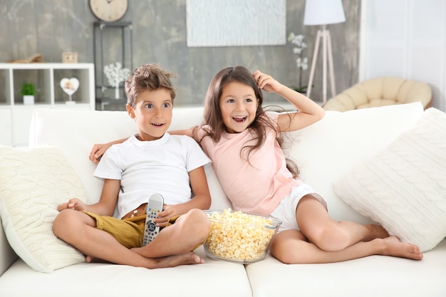 Słodkie dzieci oglądają telewizję na kanapie w domu