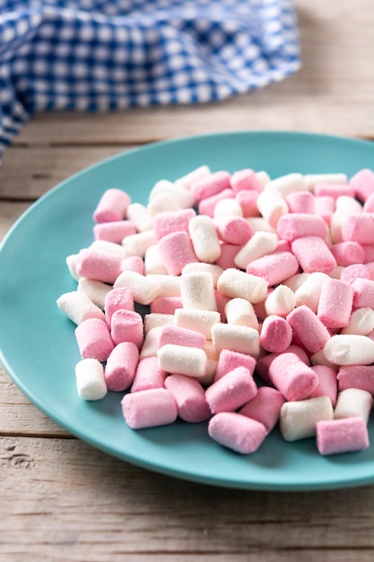 Bezpłatne zdjęcie słodkie marshmallows posypane niebieskim talerzem na drewnianym stole