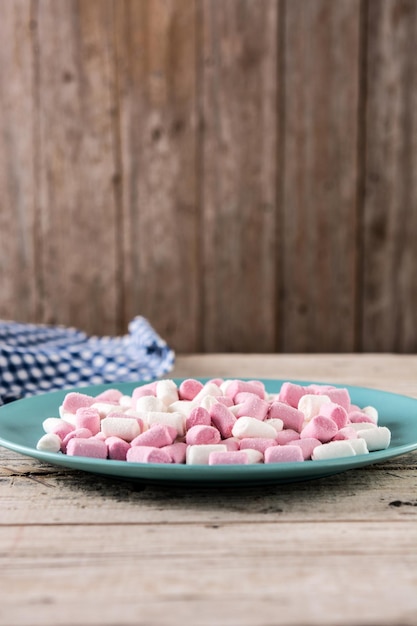 Bezpłatne zdjęcie słodkie marshmallows posypane niebieskim talerzem na drewnianym stole