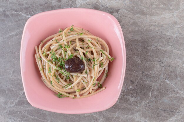 Smaczne spaghetti ozdobione zieleniną w misce w kolorze różowym.