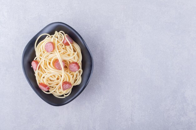 Smaczne spaghetti z pokrojonymi kiełbaskami w czarnej misce.