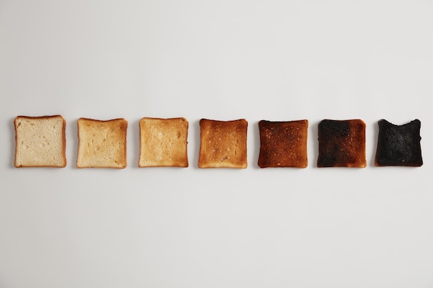 Smaczne tosty kromki chleba od nieprażonego do przypalonego. Etapy tosty. Selektywna ostrość. Chrupiąca pyszna przekąska. biała powierzchnia. Zestaw tostów każdy opiekany przez dłuższy czas, stopień upieczenia.