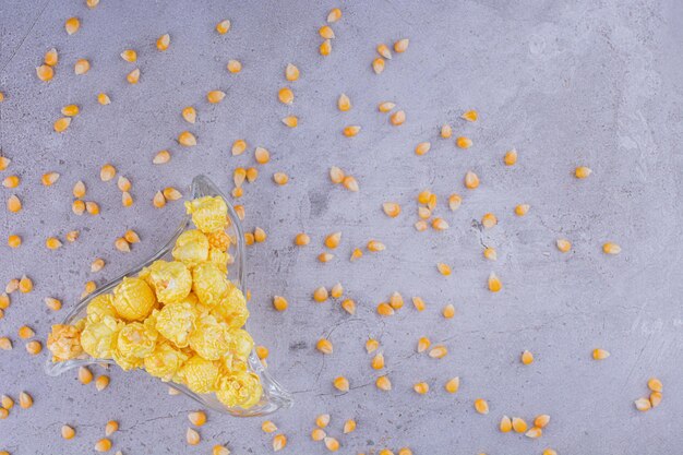 Smakowy popcorn na trójkątnym półmisku z ziarnami kukurydzy rozrzuconymi na marmurowym tle. Zdjęcie wysokiej jakości