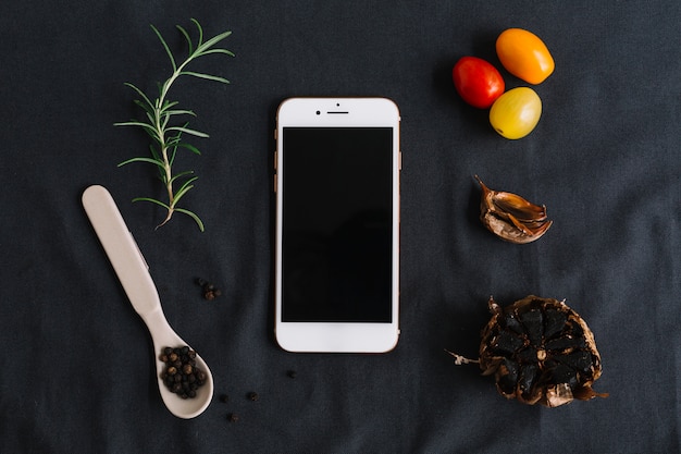 Bezpłatne zdjęcie smartphone; rozmaryn; pomidory koktajlowe; czarny pieprz i czosnek na ciemnym tle