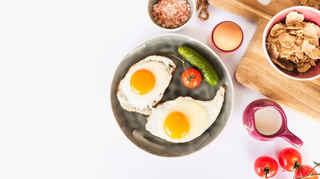 Smażący omelette z pomidorem i ogórkiem na talerzu nad białym tłem