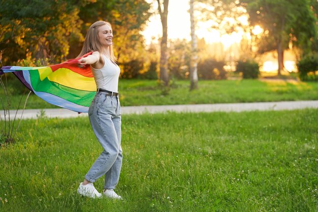 Śmiejąca się tolerancyjna kobieta tańcząca z tęczową flagą lgbt