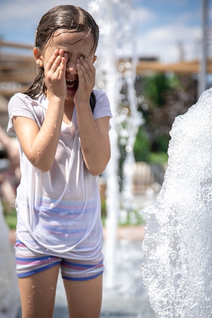 Śmieszna mała dziewczynka w fontannie, wśród rozprysków wody w upalny letni dzień.