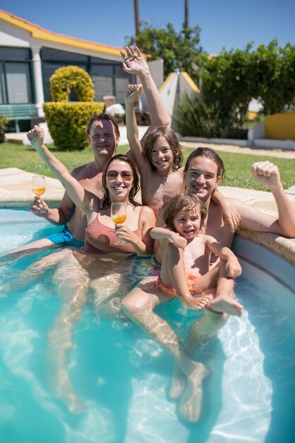 Śmieszna rodzina w basenie na podwórku. Śliczni chłopcy w różnym wieku i średnio dorośli rodzice patrzący w kamerę, uśmiechający się, podnoszące ręce. Koncepcja wypoczynku, rodziny, imprezy
