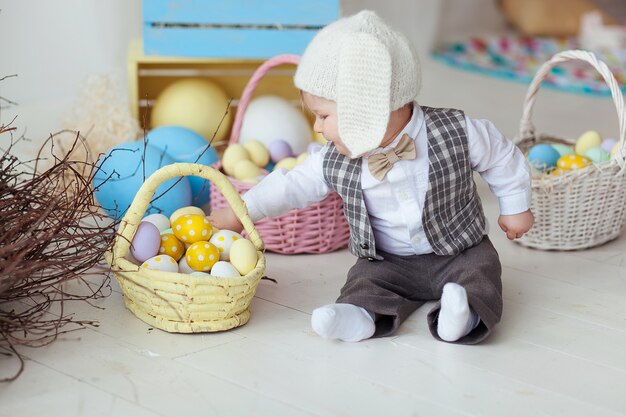 Śmieszna szczęśliwa chłopiec w kapeluszu, krawata łęku i kostiumu bawić się z Wielkanocnymi jajkami ,.