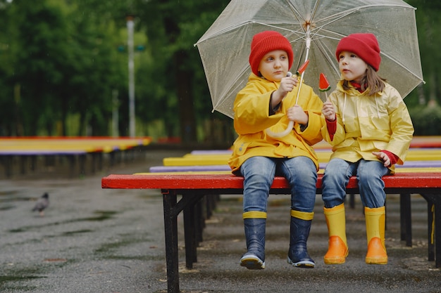 Śmieszne dzieci w kalosze bawiące się w deszczowym parku