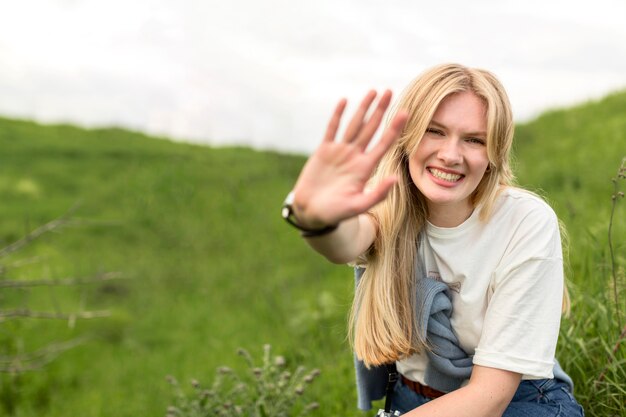 Smiley kobiety mienia ręka up podczas gdy pozujący w naturze