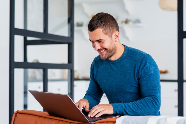 Bezpłatne zdjęcie smiley mężczyzna pracuje na laptopie od domu