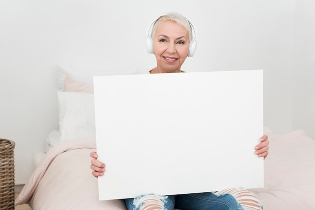 Smiley starsza kobieta jest ubranym hełmofony i trzyma pustego plakat w łóżku