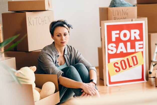 Smutna kobieta siedząca wśród swoich rzeczy po sprzedaży domu