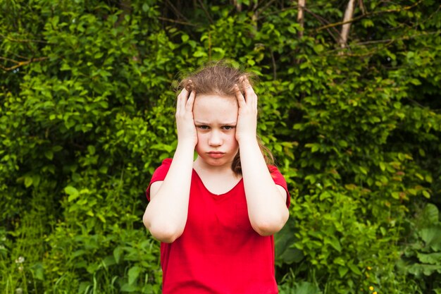 Smutny dziewczyny dziecko ma migrenę patrzeje kamery pozycję w parku