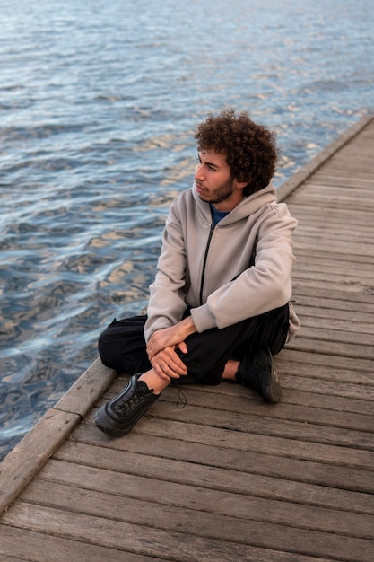 Bezpłatne zdjęcie smutny i kontemplacyjny mężczyzna siedzi nad jeziorem