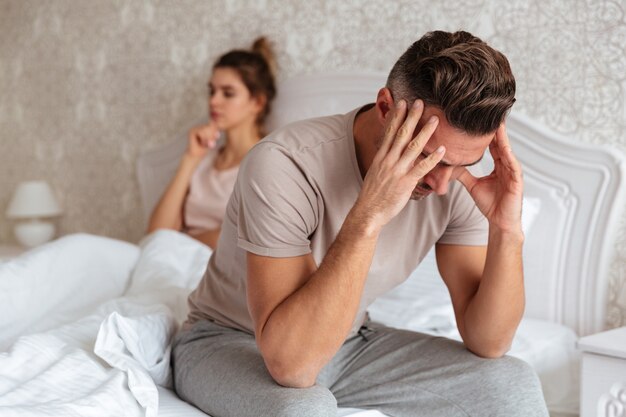 Smutny mężczyzna siedzi na łóżku ze swoją dziewczyną