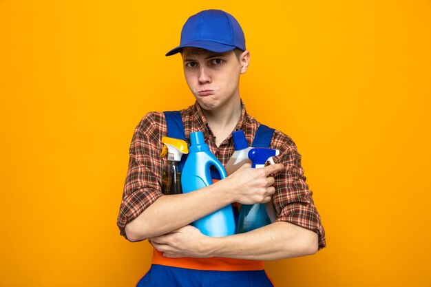 Smutny młody sprzątacz ubrany w mundur i czapkę, trzymający narzędzia do czyszczenia