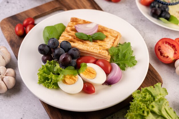Śniadanie składa się z chleba, gotowanych jajek, sosu sałatkowego z czarnych winogron, pomidorów i pokrojonej w plasterki cebuli.