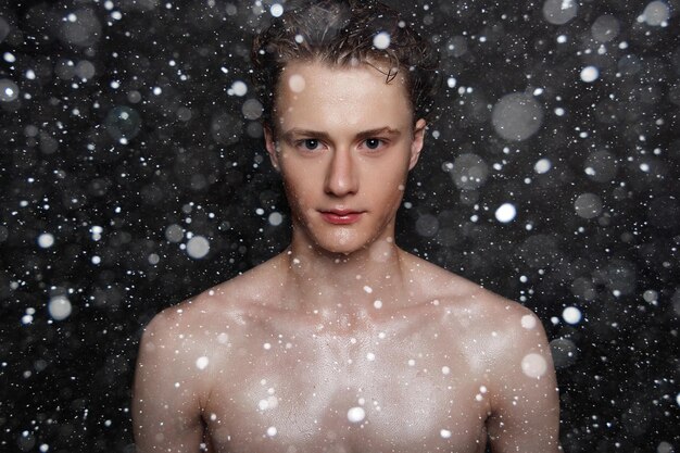 Śnieg, zima, boże narodzenie, ludzie, pielęgnacja skóry i koncepcja urody - mokry młody człowiek z czarnymi włosami na czarnym tle śniegu. portret mężczyzny z ogoloną klatką piersiową. pielęgnacja męskiej skóry.