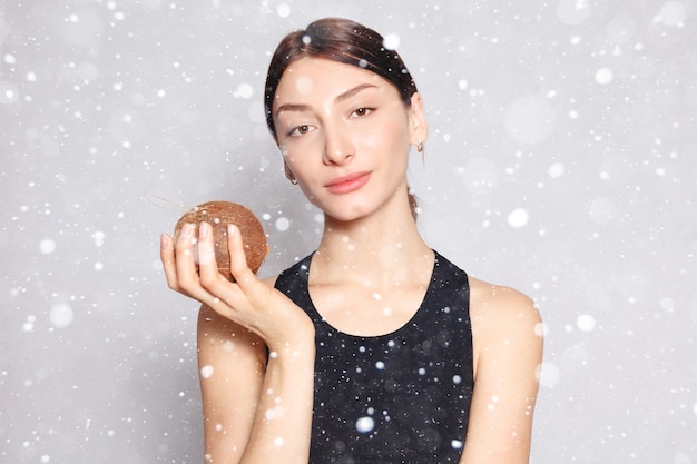 Śnieg, zima, święta, zdrowie, ludzie, jedzenie i koncepcja urody - piękna młoda dziewczyna z jasnym naturalnym makijażem i idealną skórą z kokosem w dłoni na tle śniegu
