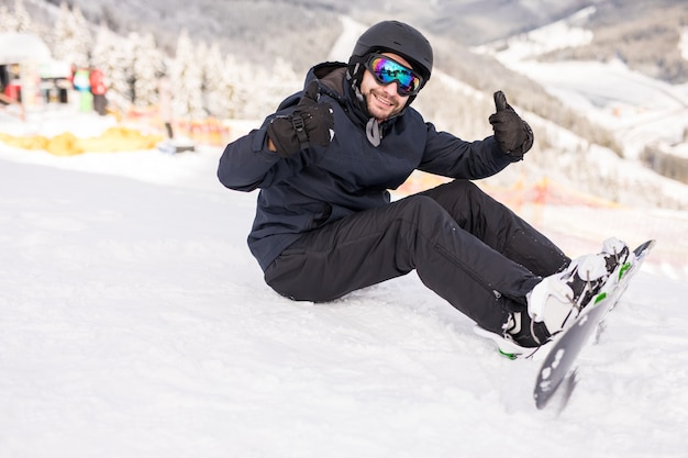 Snowboardzista siedzi wysoko w górach na skraju stoku i przed jazdą patrzy w kamerę