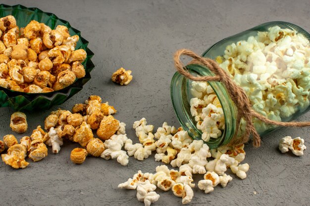 Solony popcorn ze słodkim pysznym popcornem w szklanej puszce i zielonym talerzu na szarym