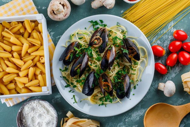 Spaghetti i omułek na talerzu z surowym makaronem, pomidorem, mąką, grzybami, drewnianą łyżką