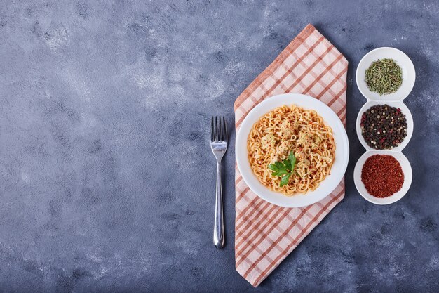 Spaghetti w białym talerzu z przyprawami dookoła, widok z góry.