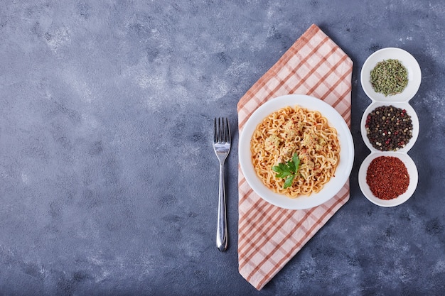 Spaghetti w białym talerzu z przyprawami dookoła, widok z góry.