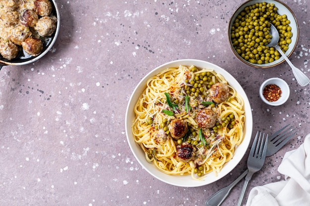 Spaghetti z kulkami mięsnymi i sosem śmietanym podawane na talerzu z ziołami i parmesanem