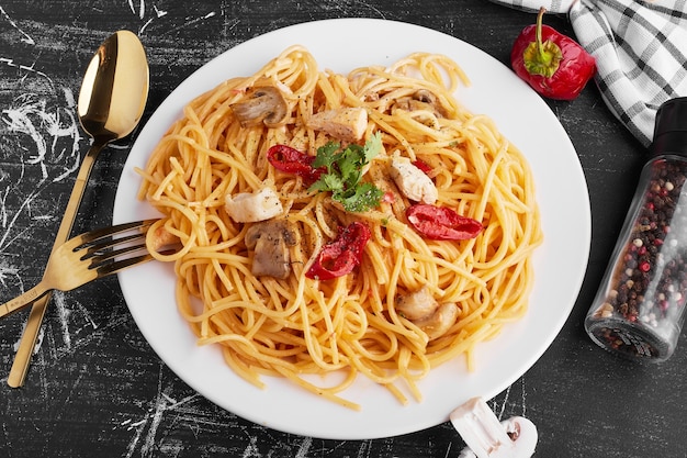 Spaghetti z mieszanymi składnikami na białym talerzu z odstawionymi sztućcami.