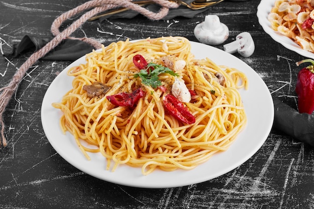 Spaghetti z mieszanymi składnikami na białym talerzu.