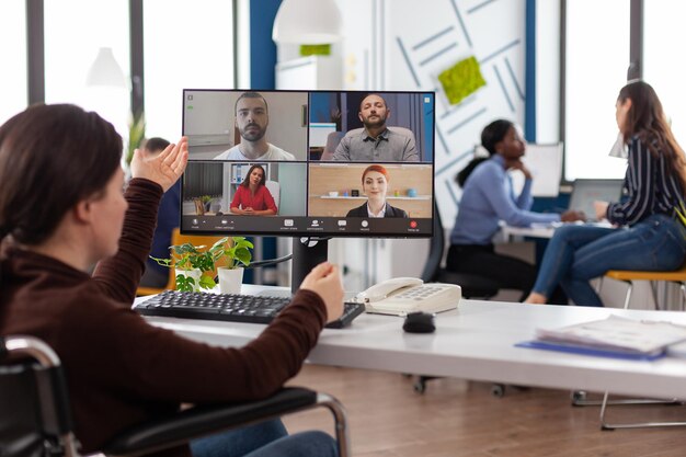 Sparaliżowana kobieta na wózku inwalidzkim omawia strategię marketingową ze zdalnym zespołem podczas konferencji online spotkanie wideorozmowy w biurze firmy. Telekonferencja na ekranie komputera