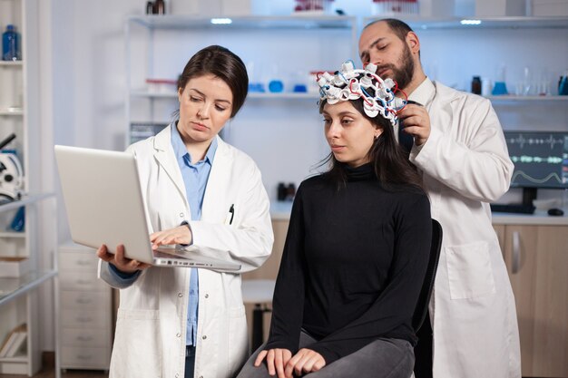 Specjalista neurolog, lekarz robi notatki na laptopie, pytając o objawy pacjenta, dostosowując zaawansowane technologicznie słuchawki eeg. Doktor naukowiec kontrolujący zestaw EEG analizujący funkcje mózgu i stan zdrowia.