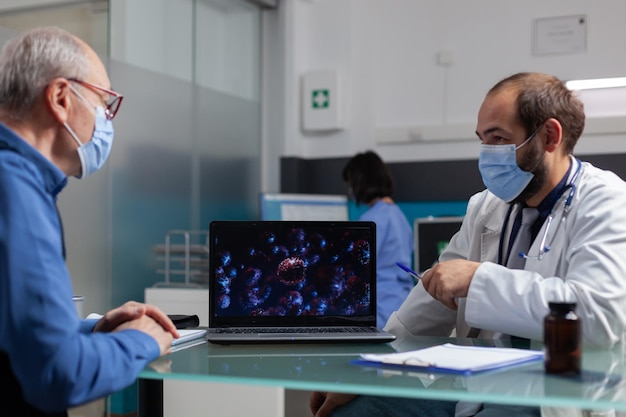 Specjalista wyjaśniający prezentację wirusa na laptopie emerytowi z maską na twarz. Lekarz opowiada o koronawirusie na wystawowej ilustracji, udzielając porady medycznej starszemu mężczyźnie.