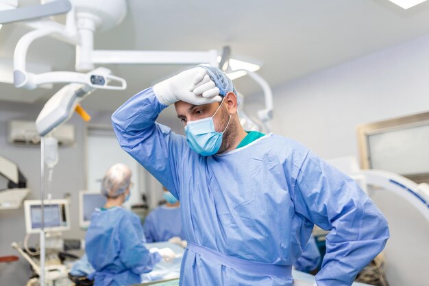Spięty chirurg z rękami na twarzy na sali operacyjnej w szpitalu, wyczerpany chirurg po długiej operacji