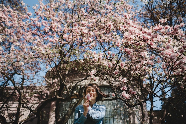 Spójrz od dołu na kobietę stojącą pod kwitnącym różowym drzewem